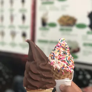 a hand holding an ice cream cone with chocolate and sprinkles