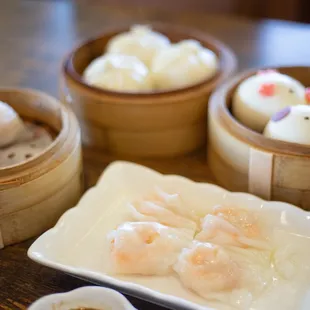 left: shrimp dumplings, top middle: steamed BBQ pork buns, right: custard buns, bottom middle: shrimp rice noodle roll with yellow chives