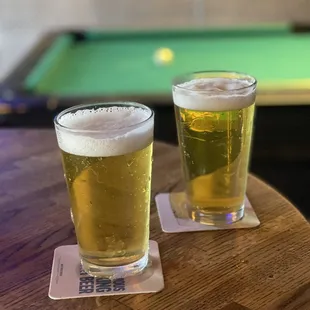 two glasses of beer and a pool table