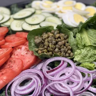 a salad with lettuce, tomatoes, cucumbers, red onions, and eggs