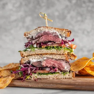 a roast beef sandwich on a cutting board with chips