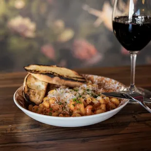 a bowl of pasta, bread and a glass of wine