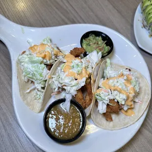 three tacos on a plate with a side of guacamole