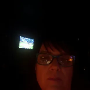 a woman with glasses and a television in the background