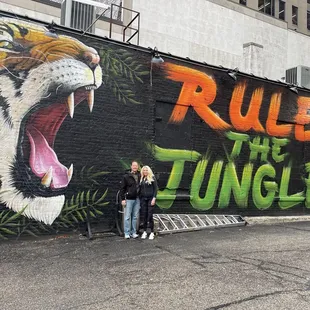 two people standing in front of a mural of a tiger