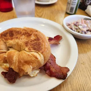 Croissant sandwich with bacon, egg, and cheese as well as a side of coleslaw.
