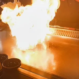 a man cooking on a grill with flames in the background