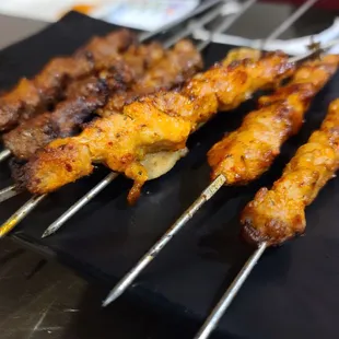 several skewered meats on a black plate