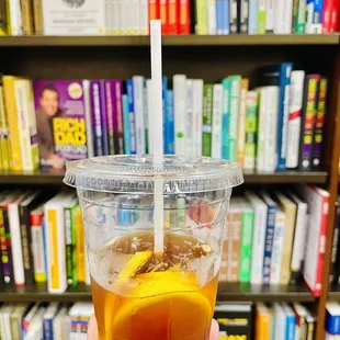 a person holding a drink in front of a bookshelf