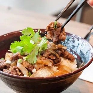 a hand holding chopsticks over a bowl of food