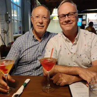 two men sitting at a table with drinks
