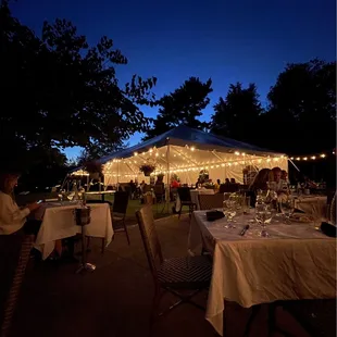 tables and chairs set up under a tent with string lights
