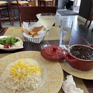 Khoresh fesenjoon (stew and rice) in the foreground, complimentary appetizer plate with bread at rear, and the Azadi cocktail.