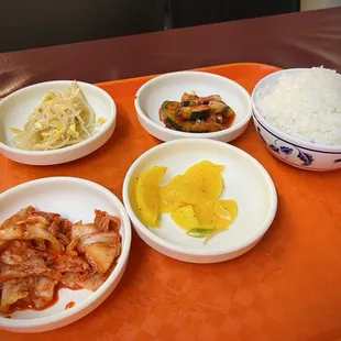 Top left to right: bean sprouts, spicy cucumbers, steamed white rice.  Bottom left to right: kimchi, yellow radish