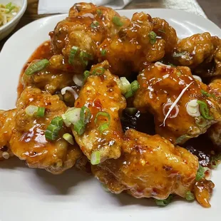 a plate of chicken wings with sauce and green onions