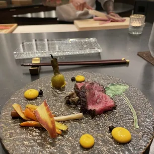 a plate of food on a table with a chef in the background