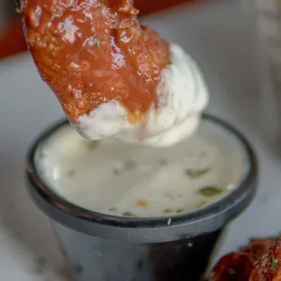 a hand dipping a piece of fried chicken