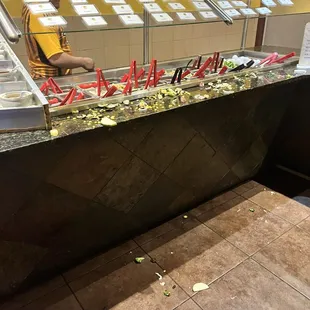 Raw food and vegetables are scattered on the counters and floor of Mongolian grill.