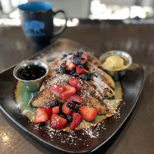 a plate of french toast with berries and powdered sugar
