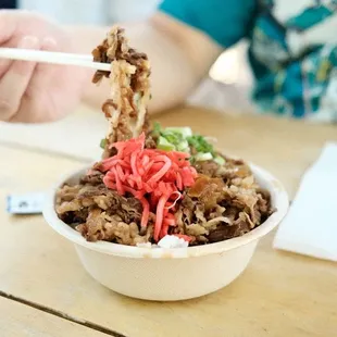 a person eating a bowl of noodles with chopsticks