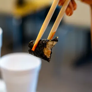 a person holding chopsticks over a piece of sushi