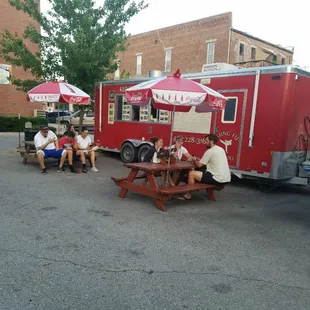 people sitting at picnic tables in front of a food truck