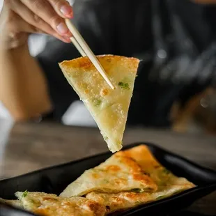 a person holding chopsticks over a piece of food