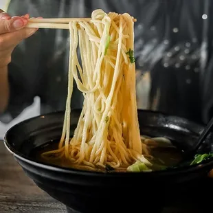 a woman holding chopsticks over a bowl of noodles