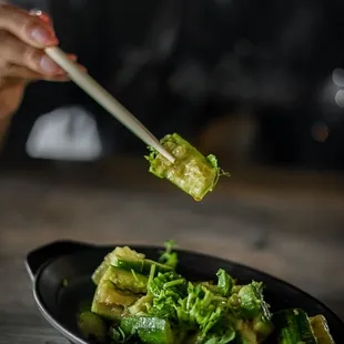 a person holding chopsticks over a plate of broccoli