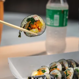 a person holding chopsticks over a plate of sushi