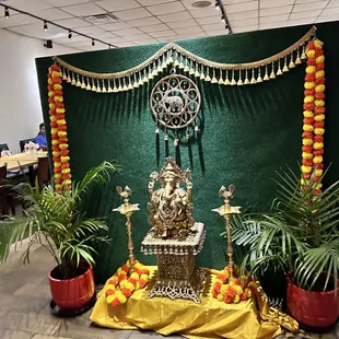 a green backdrop with a gold statue and potted plants