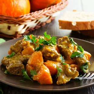 a plate of stew with bread and oranges in the background