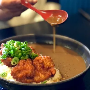 a person dipping sauce over a bowl of food
