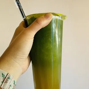 a hand holding a cup of green juice