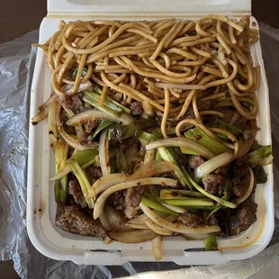 a take out box of noodles and beef