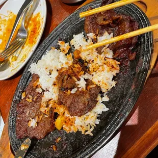 a platter of meat and rice with chopsticks