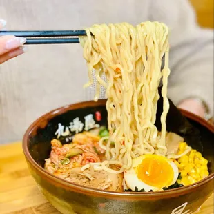 a person holding chopsticks over a bowl of ramen