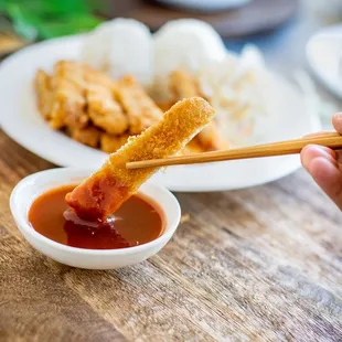 a person holding chopsticks and dipping sauce