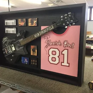 Rick Springfield autographed guitar and shirt resting beneath a simple black shadow box frame.