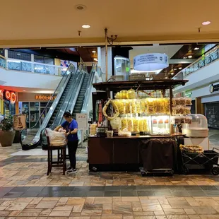 Located on the ground level near the escalator on the Ross and Regal Cinema wing