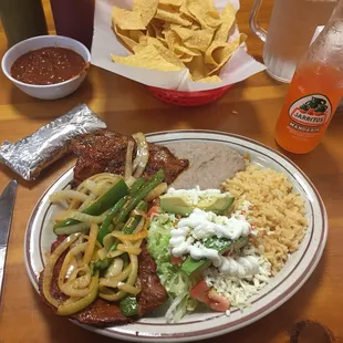Marinated Pastor Enchilada with rice, beans, tortillas, avocado, lettuce and jalapeños and a Jarritos Mandarin orange soda.  Delicious