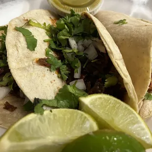 two tacos on a plate with lime wedges