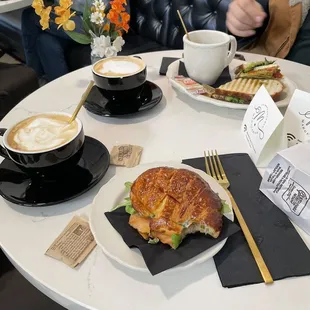 Two cappuccinos, salmon croissant sandwich, and soup and sandwich combo.