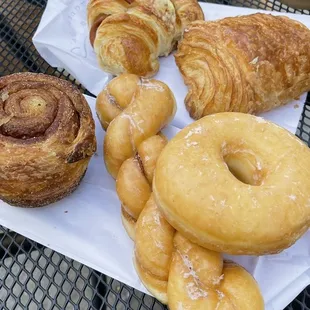 Front left to right: morning bun, raised glazed twist, raised glazed  Back, left to right: ham and cheese croissant, chocolate croissant