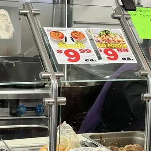 a woman behind a counter with a variety of food items