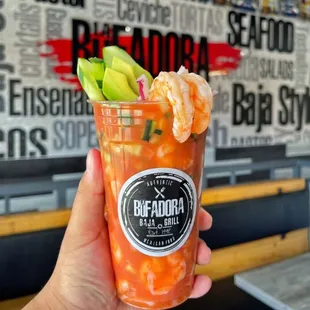 a hand holding a glass of bloody shrimp