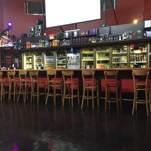a bar with red chairs and a large screen