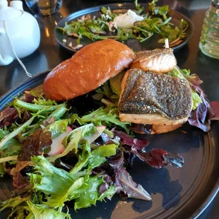 Salmon sandwich with avacado on a light brioche bun and mixed greens salad.