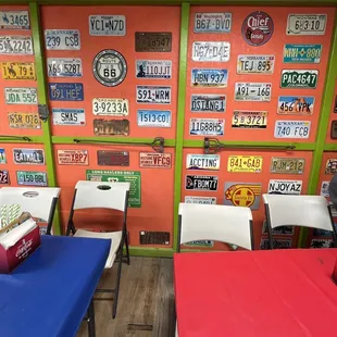 tables and chairs in front of a wall of license plates