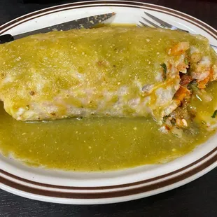 Wet al pastor burrito with green sauce filled with meat and rice.
